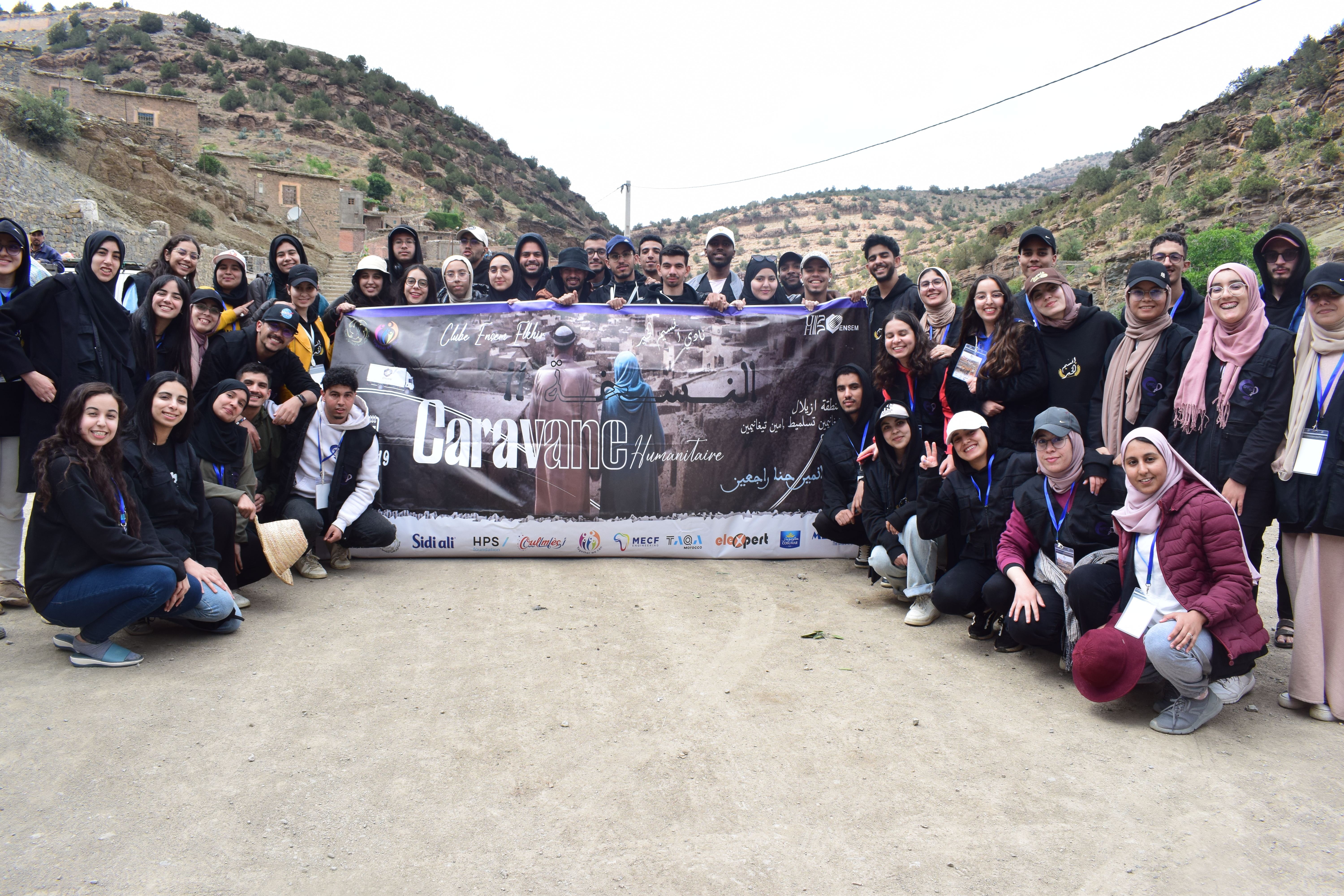 Groupe de jeunes posant avec une banderole de caravane humanitaire dans un paysage rural.